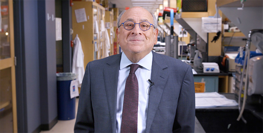Man wearing a suit and glasses smiling with a lab behind him.