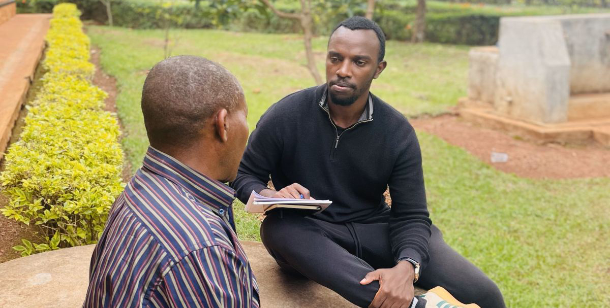 Two men sitting on a concrete stoop; one holding a notebook.