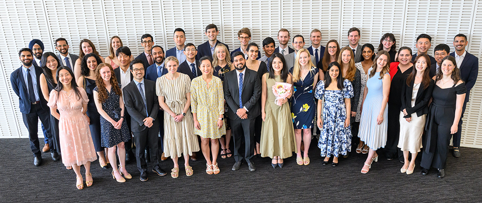 Photo of many students smiling with white wall in background