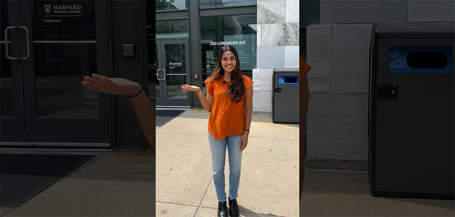 Ria Goyal standing in front of a building with her hand up.