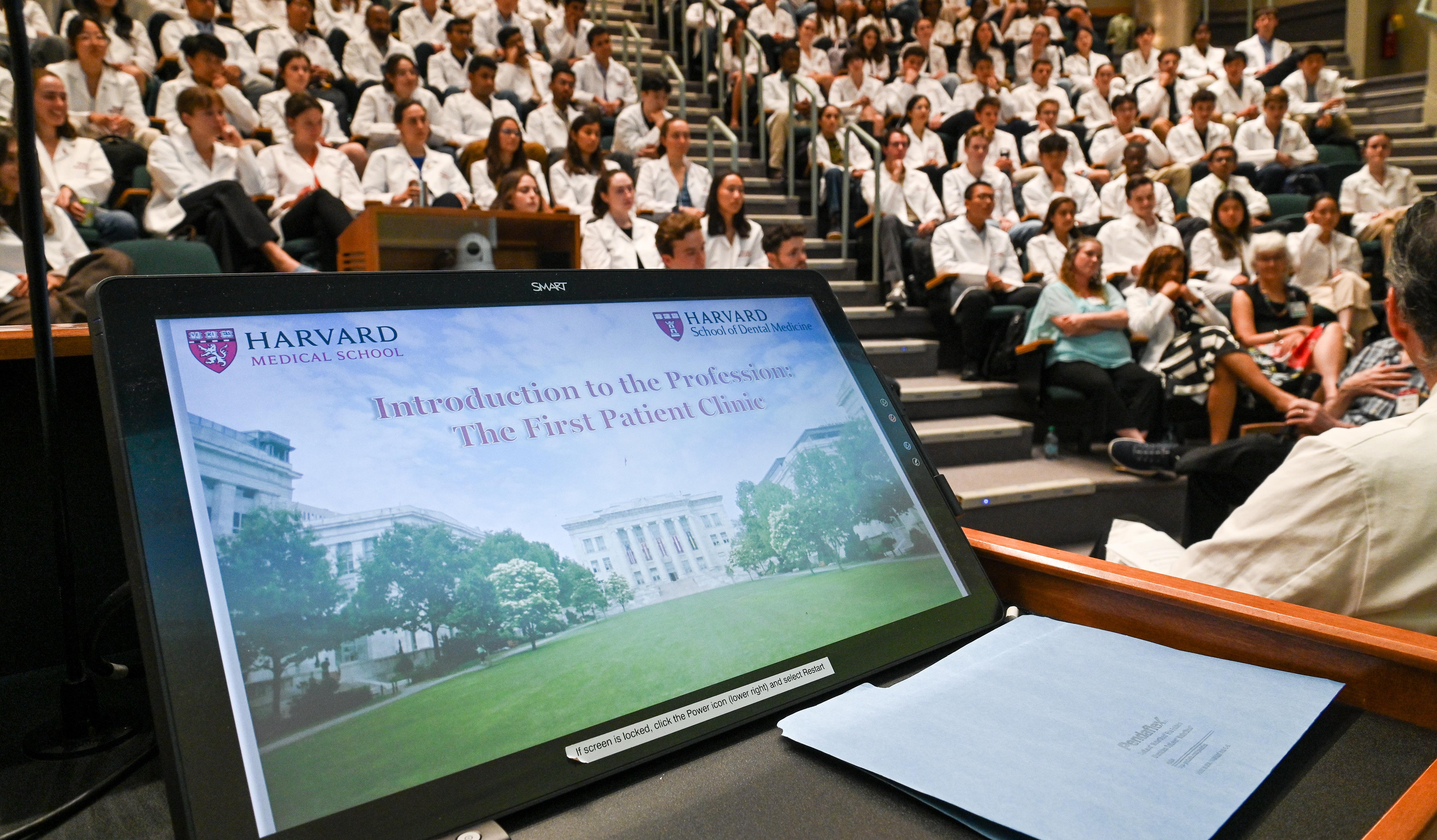 Laptop screen with the words "Introduction to the Profession" and an auditorium of students wearing white coats.