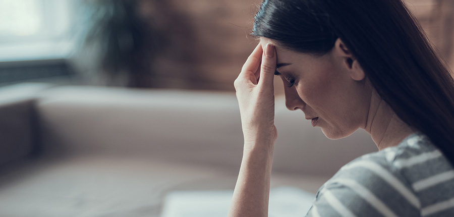 Brunette woman in living-room expressing head pain and sadness.