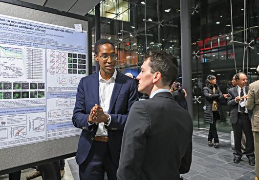 Samuel Zinga (left), a student trainee  in the Harvard/MIT MD-PhD Program,  discusses his research at a poster  session held during the program's  50th anniversary celebration Nov. 15.