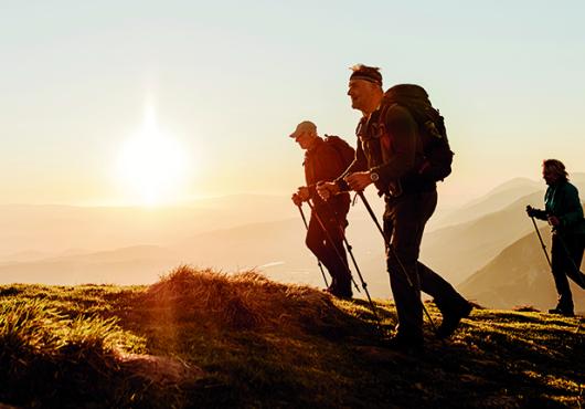 Three older people hiking with walking sticks on a mountain.