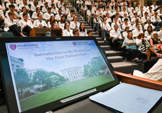 Laptop screen with the words "Introduction to the Profession" and an auditorium of students wearing white coats.