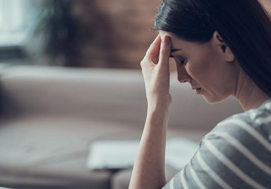 Brunette in living room expressing sadness and head pain.