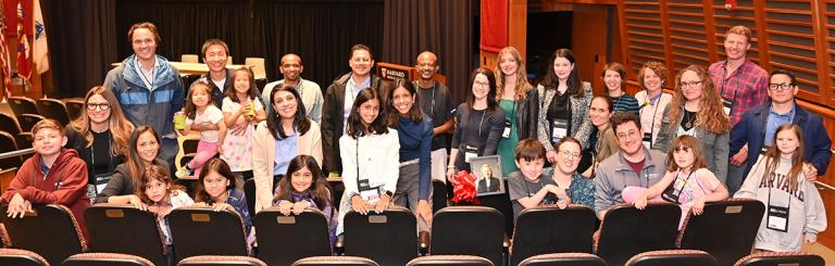 Large group of alumni clustered around chairs in an auditorium.