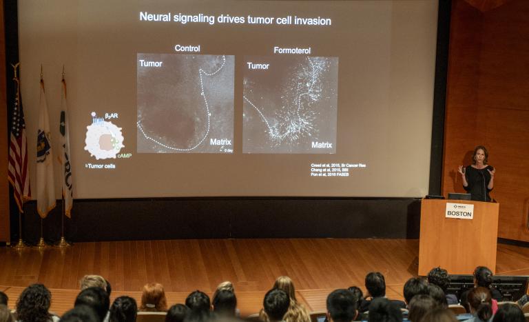 Woman at a podium with a large screen behind her.