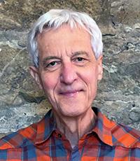 Man in plaid shirt standing in front of a stone wall.