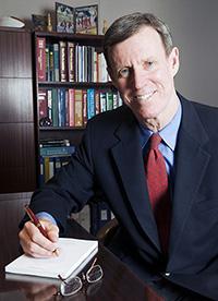 Man wearing a suit writing in a notebook and smiling.
