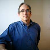 Man wearing glasses standing in front of a wall, half of which is covered with scientific notes.