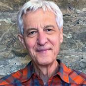 Man in plaid shirt standing in front of a stone wall.