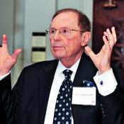 M. Lee Pearce wearing a suit and glasses with his hands held up.